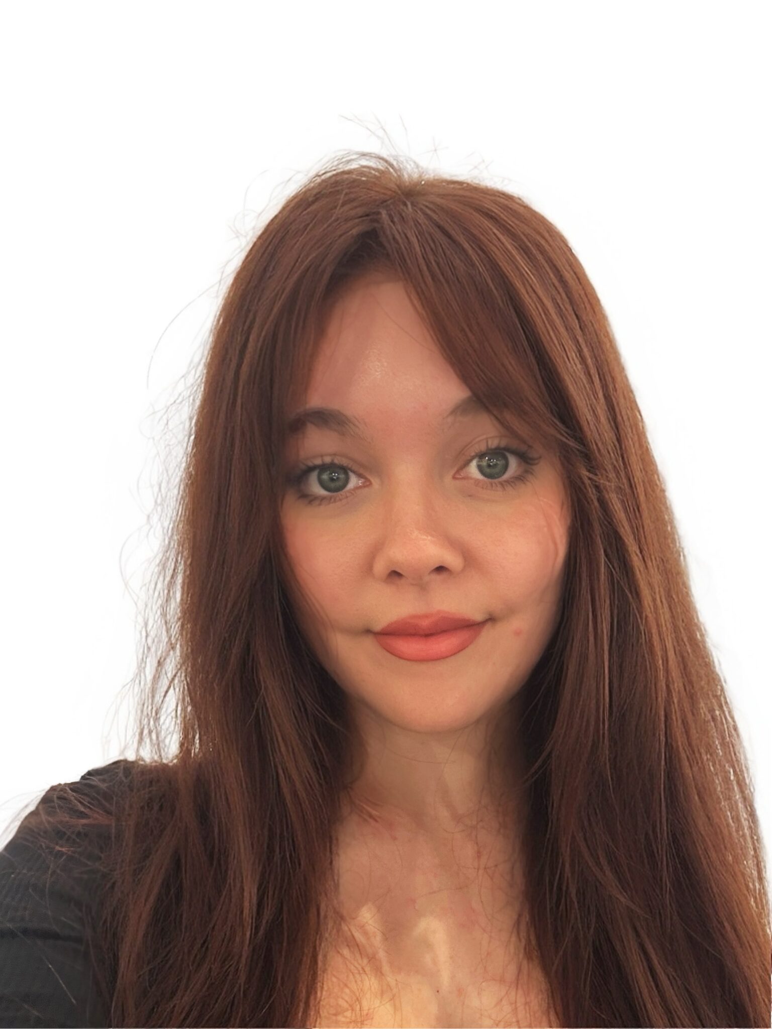 Close-up of a young woman with long brown hair and green eyes against a white background, wearing a dark top.